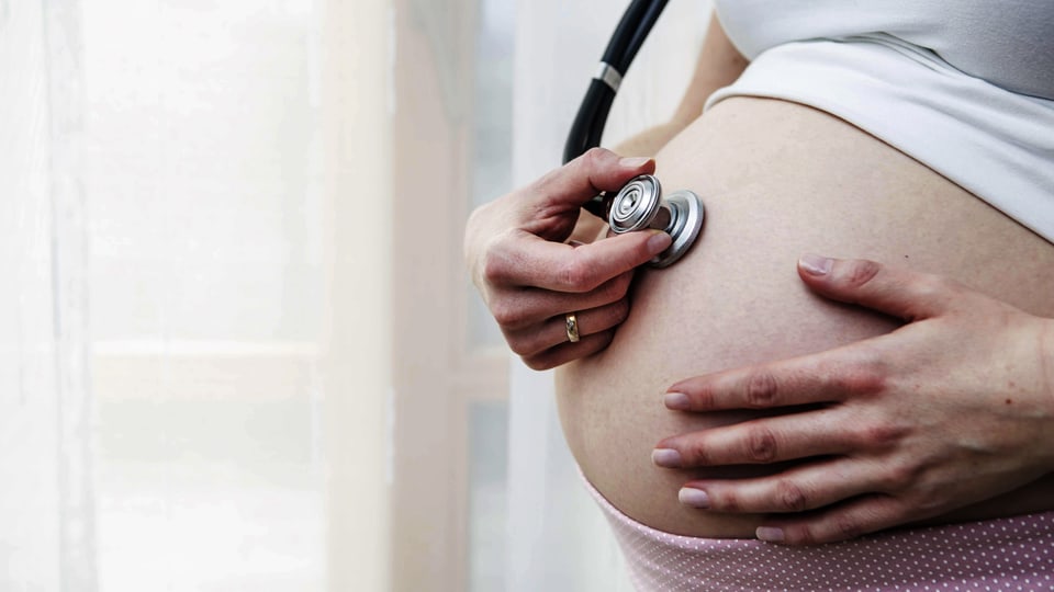 Symbolbild: Eine Schwangere hört ihren Bauch mit einem Stethoskop ab.