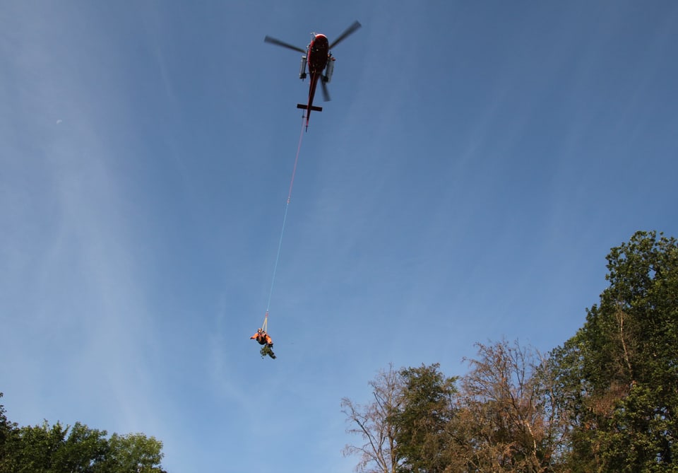 Ein Helikopter fliegt und ein Mann hängt an einem Seil.