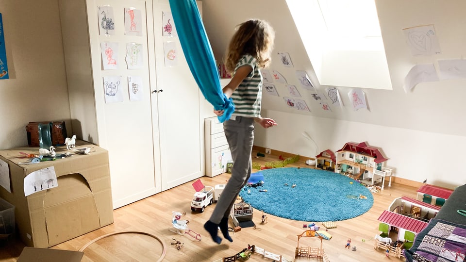 Ein Mädchen hält ein blaues Tuch und hüpft im Zimmer umher