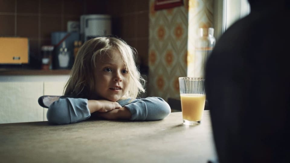 Filmszene: Ein kleines Mädchen sitzt am Tisch .