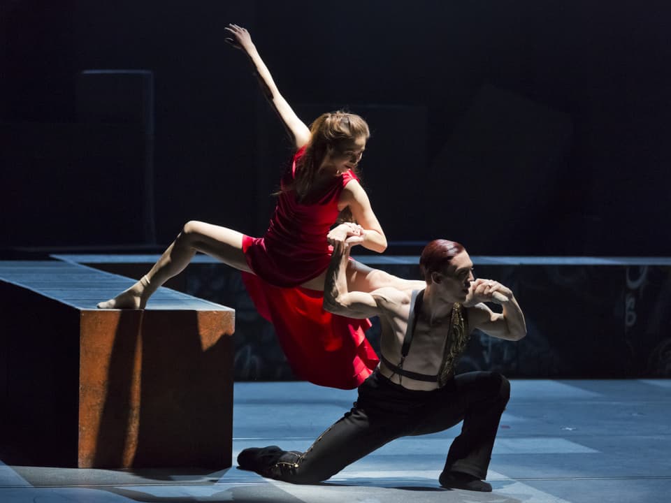 Ein Duo tanzt auf einer Theaterbühne. Das Bein der Frau liegt auf der Schulter des Mannes. 