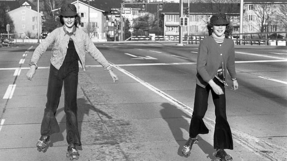 Zwei junge Mädchen geniessen beim Rollschuhlaufen die leeren Strassen an einem autofreiem Sonntag im November 1973 .