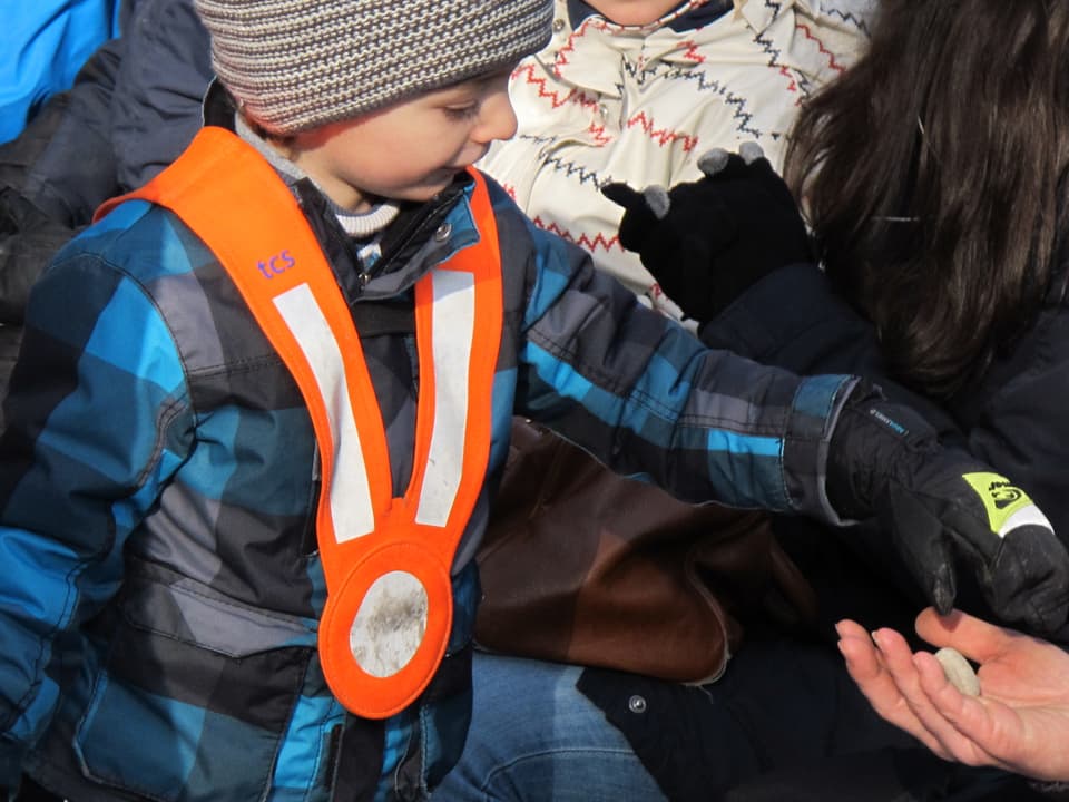 Ein Kindergartenkind reicht einer Person einen heissen Stein.