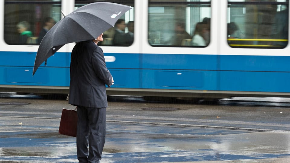 Mann in Anzug und mit Aktentasche und offenem Regenschirm vor einem Zürcher Tram.