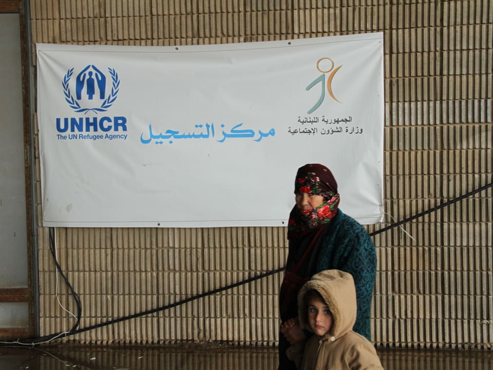 Eine Frau mit Kopftuch und ihre Tochter stehen vor einerm Plakat der Uno.