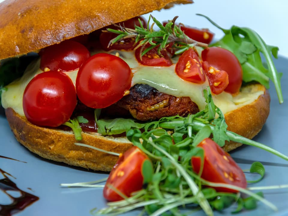 Ein Hamburger mit Cherrytomaten, Käse, Rucola und Käfern.