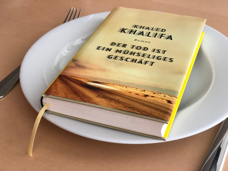 Der Roman «Der Tod ist ein mühseliges Geschäft» von Khaled Khalifa liegt auf einem weissen Teller