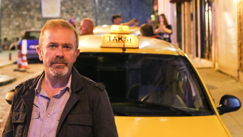 Der Taxifahrer steht vor seinem gelben Taxi.
