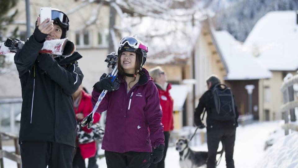 Chinese und Chinesin mit Ski auf der Schulter, sie machen ein Selfie.