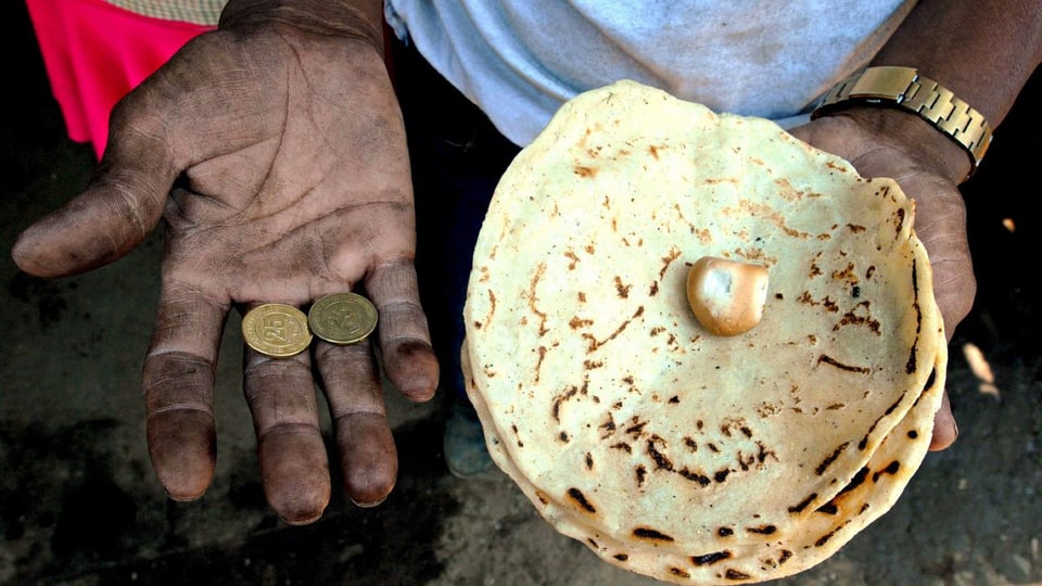 Ein Mann aus Nicaragua hält in der einen Hand Münzen, in der anderen ein Fladenbrot.