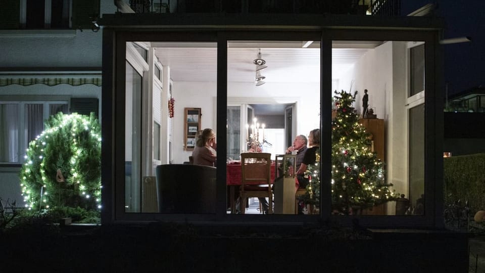 Eine Familie sitzt im Wintergarten am Tisch neben einem Christbaum.