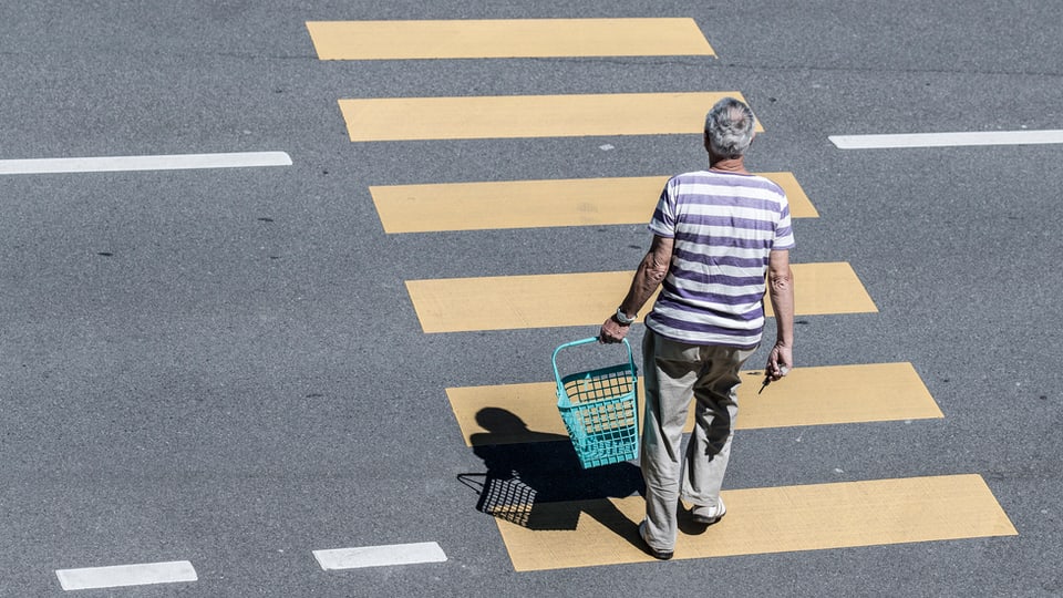 Ein Mann geht mit Einkaufskorb in der Hand über einen Fussgängerstreifen.
