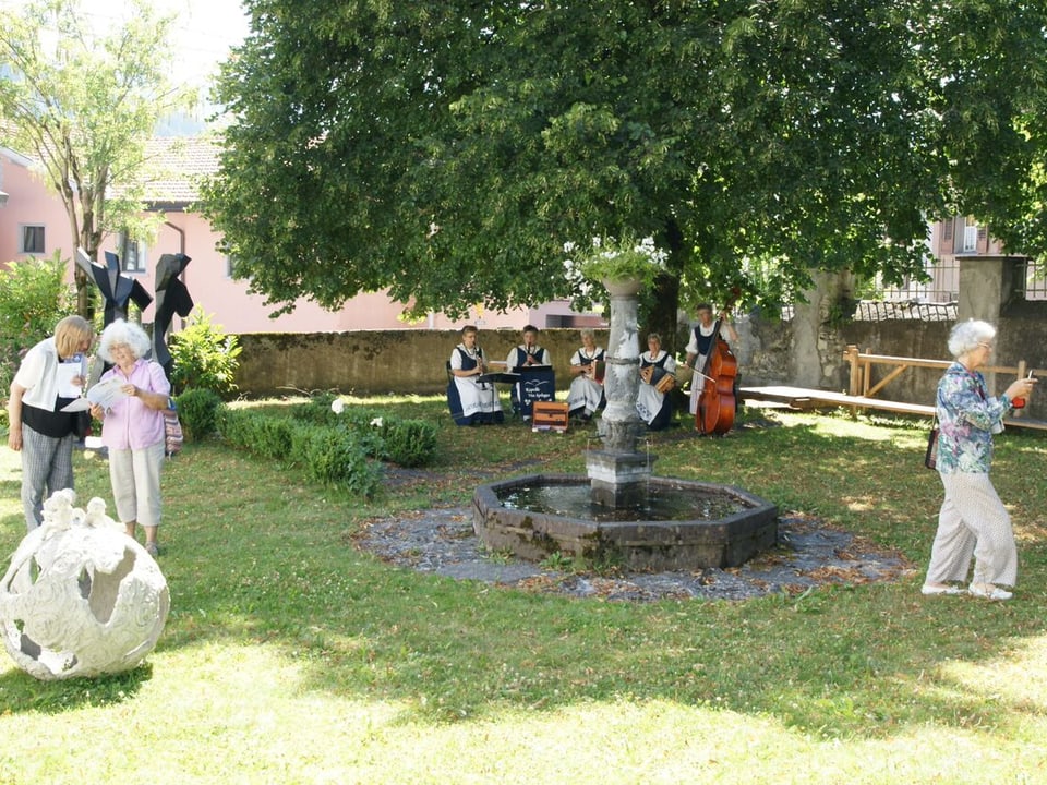 Lustwandelnde Museumsbesucherinnen im Museumsgarten. Kapelle spielt unter Baum.