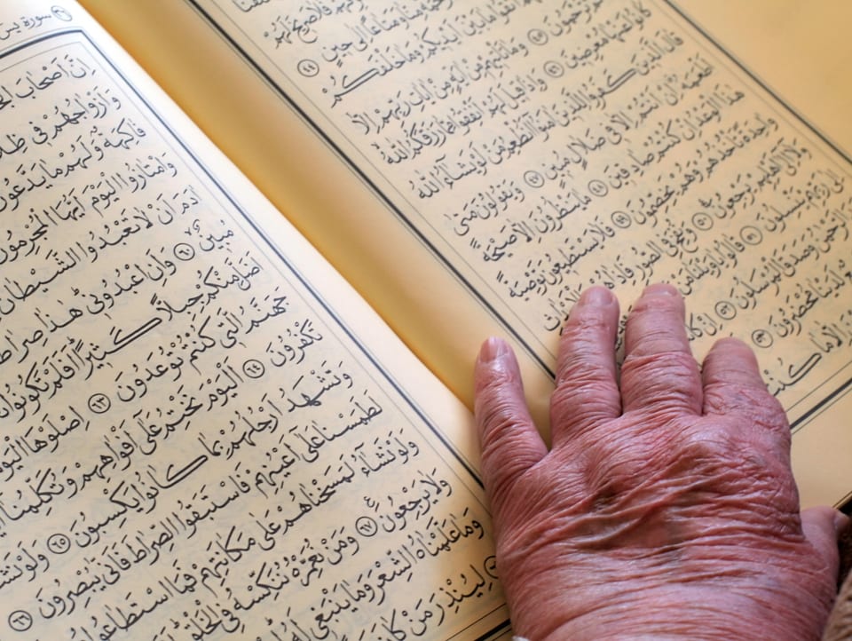 Hand einer alten Person liegt auf dem Koran
