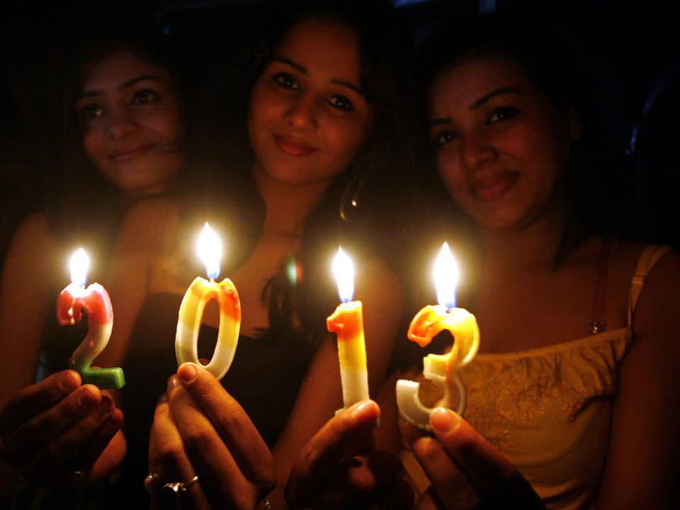 Drei Frauen in Indien halten Kerzen in der Zahlenkombination 2013. (keystone)