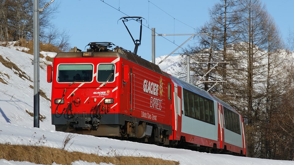 Ein Zug mit roter Lok fährt durch eine verschneite Landschaft.
