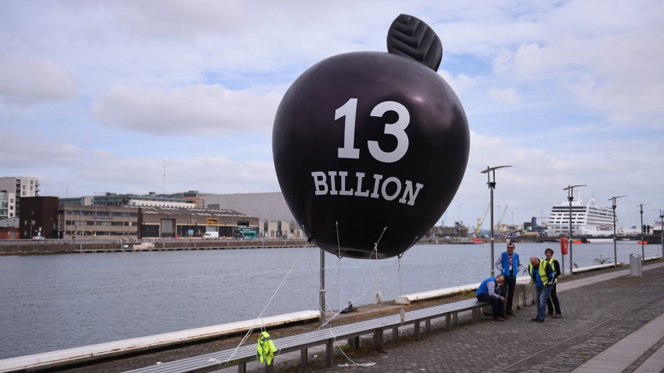 Ein schwarzer Ballon in Form eines Apfels mit der Aufschrift «13 Milliarden» ist an einer Brücke befestigt.