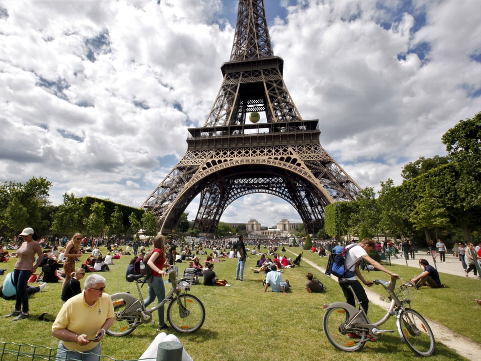 Touristen liegen auf einer Rasenfläche vor dem Eiffelturm. 