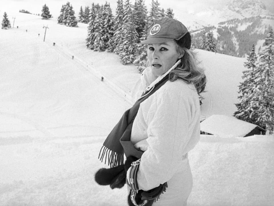 Eine Frau in weissem Skianzug steht vor einer Skipiste.