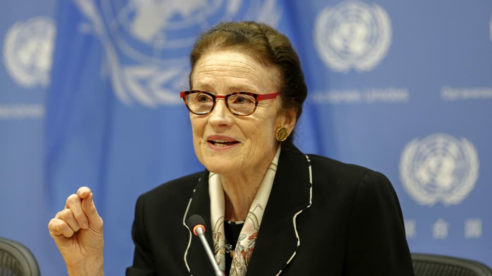 Eine ältere Frau vor einem blauen Hintergrund am Mikrofon.