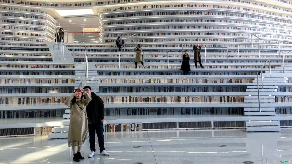 Grosser Raum mit riesigen, mehrstöckigen weissen Bücherregalen. Mehrere PErsonen sind zu sehen, die mit Handys Fotos machen.
