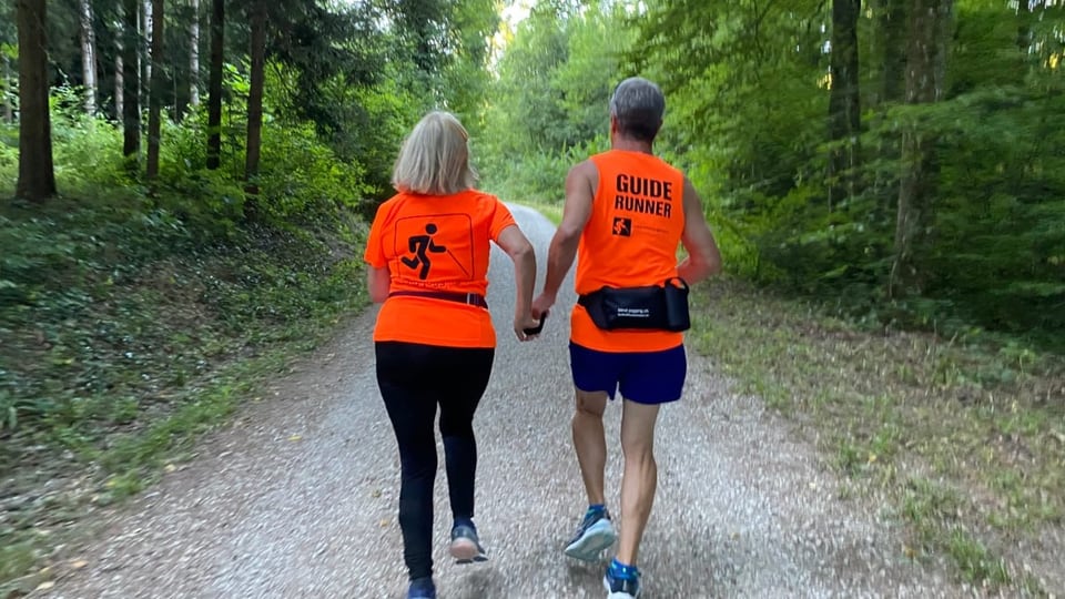 Beatrice Acuña und René Scheidegger von hinten mit orangen T-Shirts