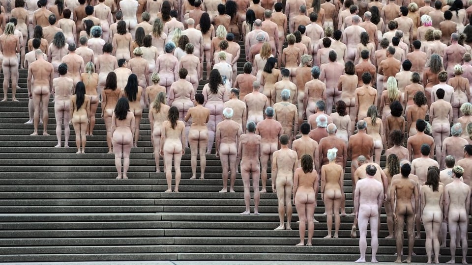 Das Bild zeigt vollkommen nackte Menschen von hinten, die nebeneinander und hintereinander auf Treppenstufen des Opernhauses in Sidney aufgereiht sind.