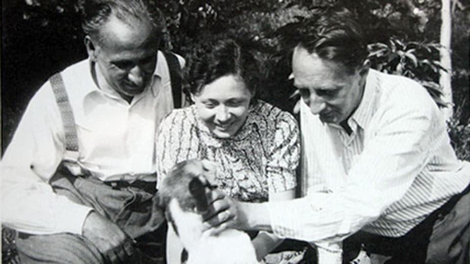 Eine junge Frau zwischen zwei älteren Herren streichelt einen Hund.