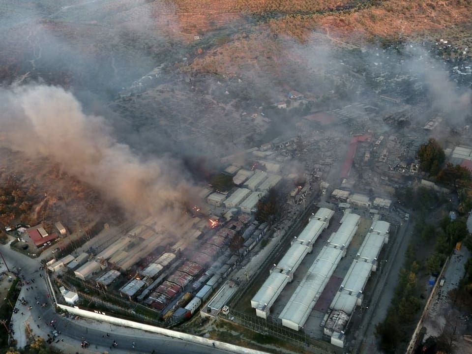 Das zerstörte Flüchtlingslager aus der Luft gesehen, Rauchschwaden steigen auf.