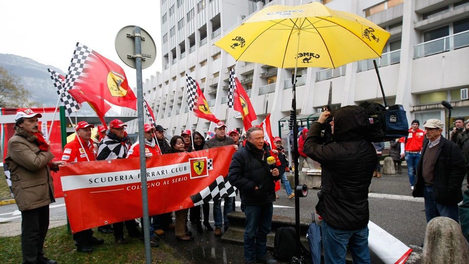 Ein Reporterteam dreht vor einer Gruppe Schumacher-Fans.