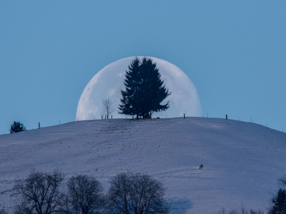 Der Mond verschwindet hinter einem schneebedeckten Hügel.