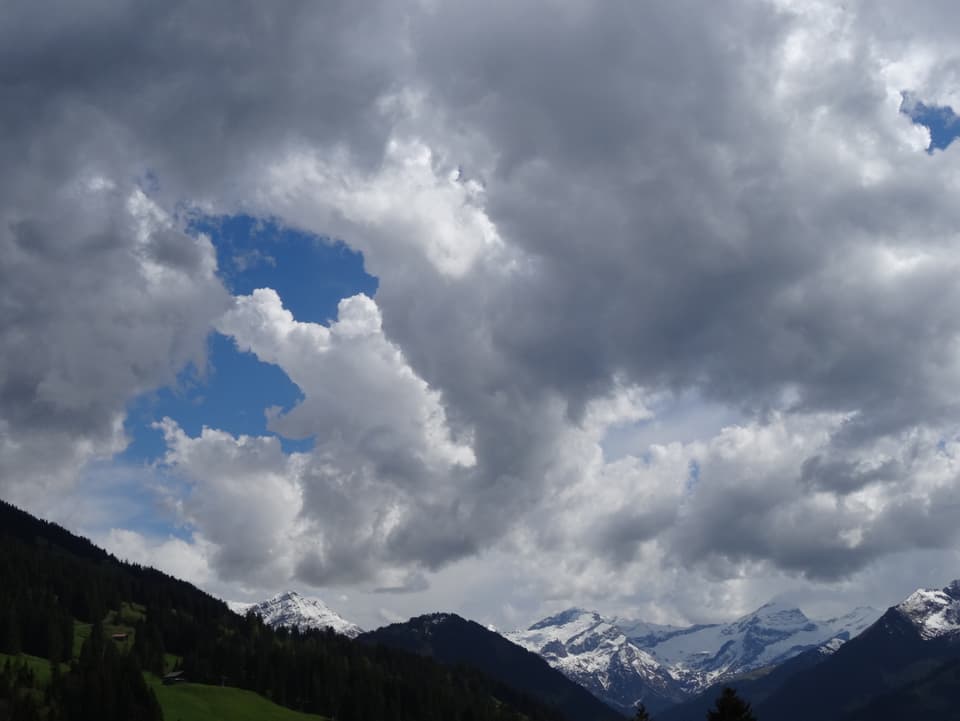 Alpen am unteren Bildrand angeschnitten. Man sieht viel vom Himmel, der bewölkt ist. Die Wolken türmen sich in die Höhe. 