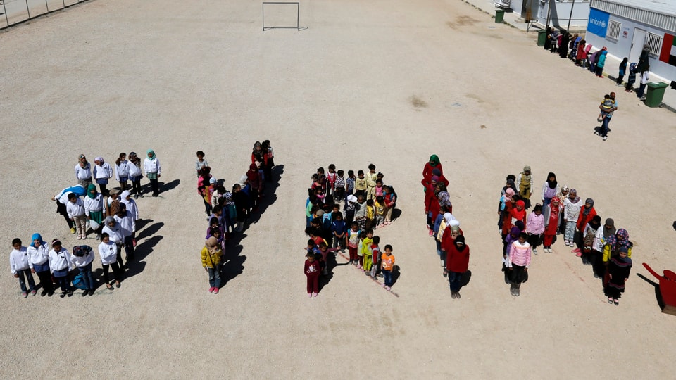 Kinder formen auf einem Platz das Wort SYRIA.