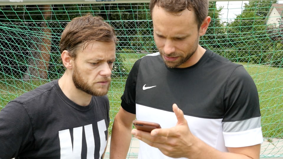 Zwei Männer schauen gebannt auf ein Smartphone.