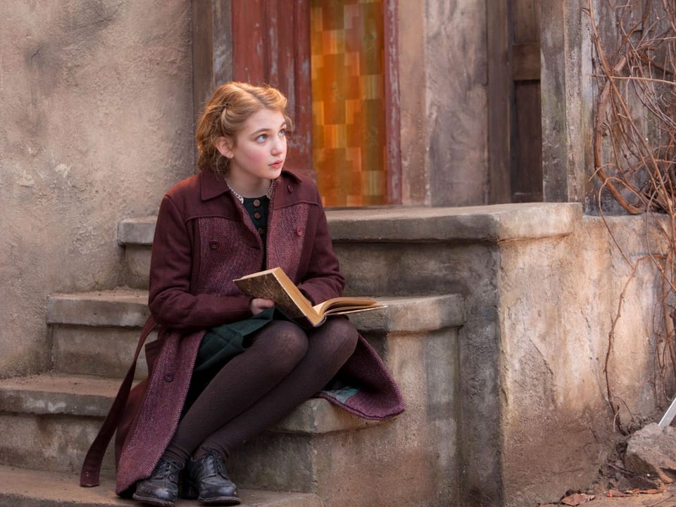 Mädchen sitzt auf Treppenstufen mit einem Buch auf den Knien.