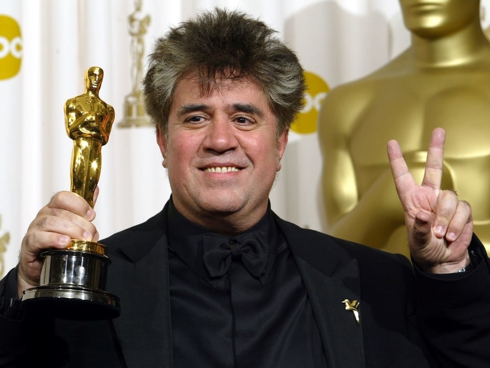 Almodovar mit seinem Oscar in der Hand und ein Peace-Zeichen formend mit der anderen. 