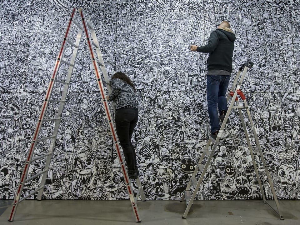 Zwei Personen arbeiten auf Leitern an einer Wandmalerei