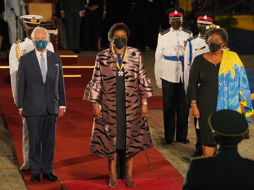 Die neue Präsidentin Barbados' geht flankiert von Prinz Charles und der Premierministerin über einen roten Teppich.