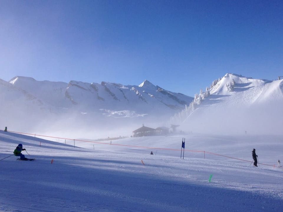 Skifahrer auf der Piste bei blauem Himmel, einzelne Nebelschwaden sind aber vorhanden.