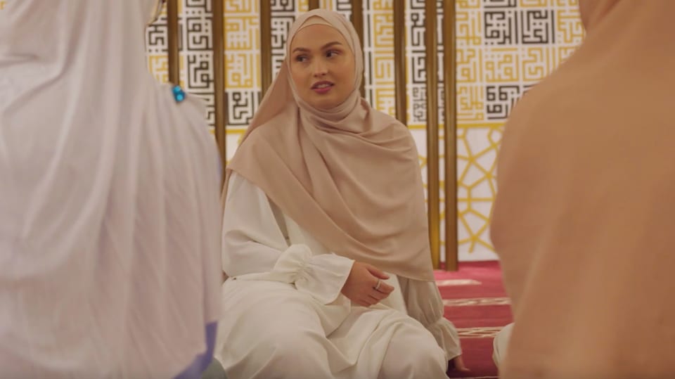 Nina im weissen Gewand und mit beigem Kopftuch in der Moschee schaut zu zwei Freundinnen.