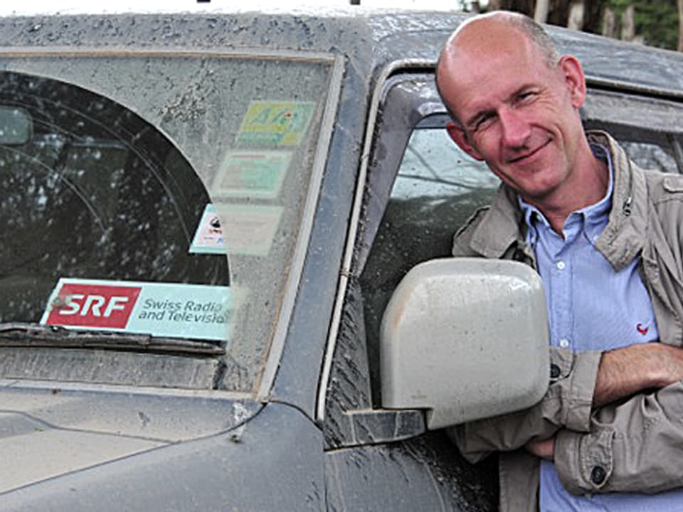 Patrik Wülser posiert neben seinem Auto mit SRF-Aufkleber an der Windschutzscheibe.