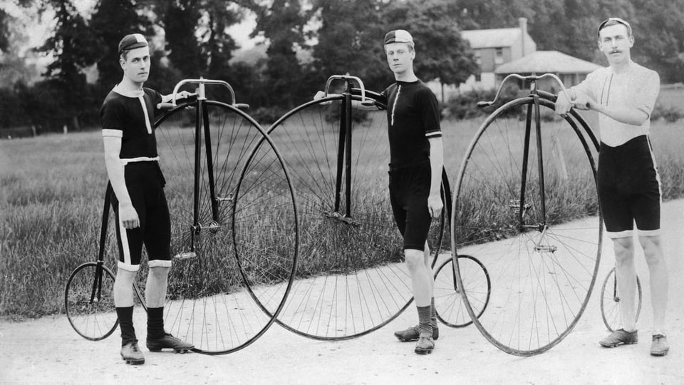 Drei Besitzer eines Penny Farthings posieren in Radler-Outfit und mit ihren Rädern.