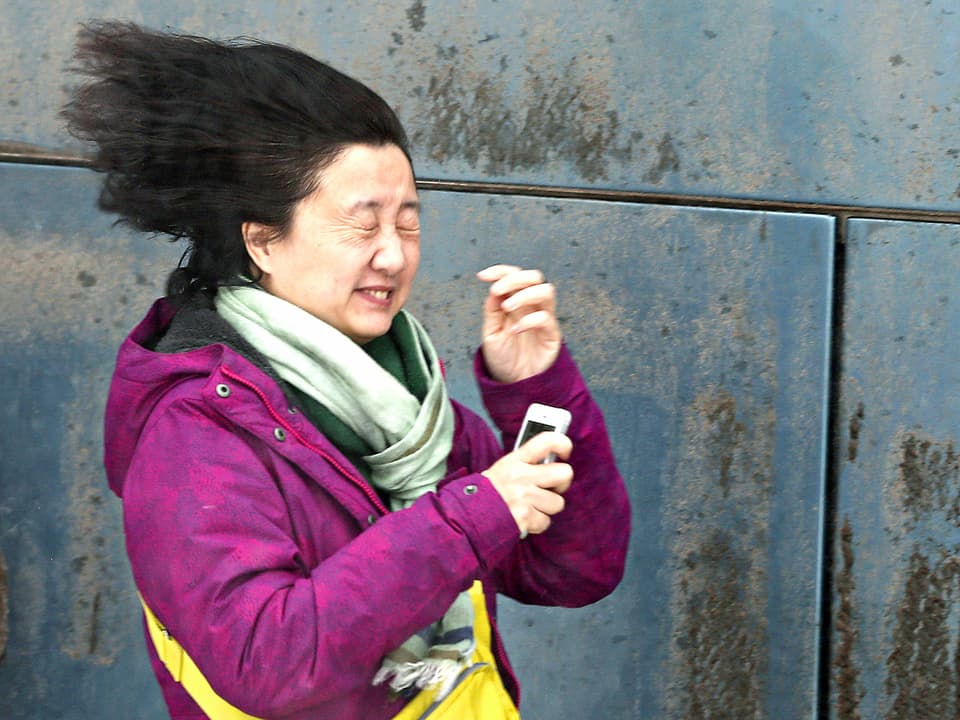 Eine asiatische Frau steht in Quebec in einer steifen Bö. Sie kneift die Augen zusammen und ihre langen Haare flattern im Sturm.