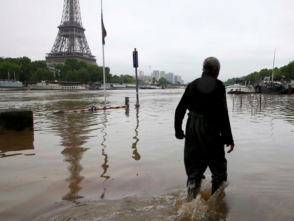 Mann watet durchs Wasser. Im Hintergrund der Eiffelturm.