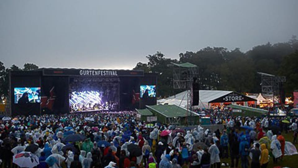 Die Hauptbühne des Gurtenfestival mit schwarzem Himmel und Besuchern in Regenschützen.