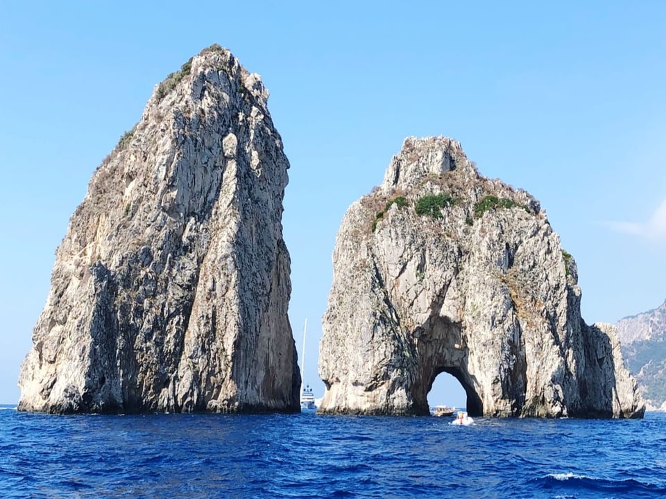 Zwei Felsen ragen vor blauem Himmel aus dem Meer hinaus