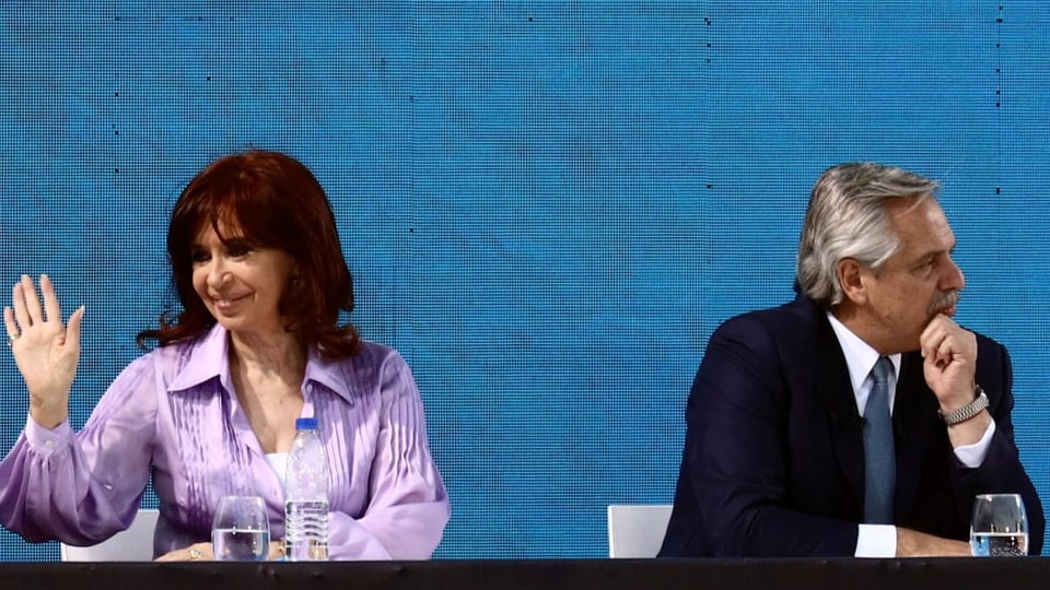 Cristina Kirchner sitzt neben Alberto Fernández und winkt.
