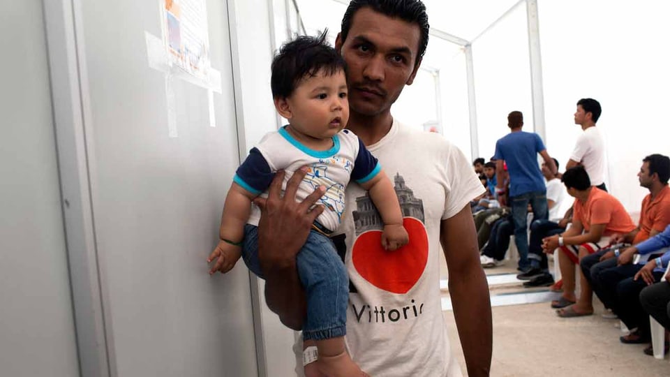 Ein Mann wartet in Griechenland im Aufnahmezentrum mit seinem Baby.