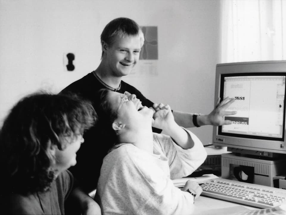 Drei junge Menschen sitzen lachend vor einem Computer