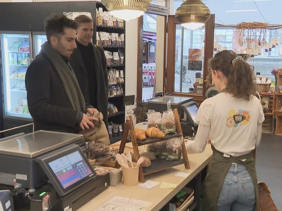 Eine Frau bedient zwei Männer an einer Ladentheke.